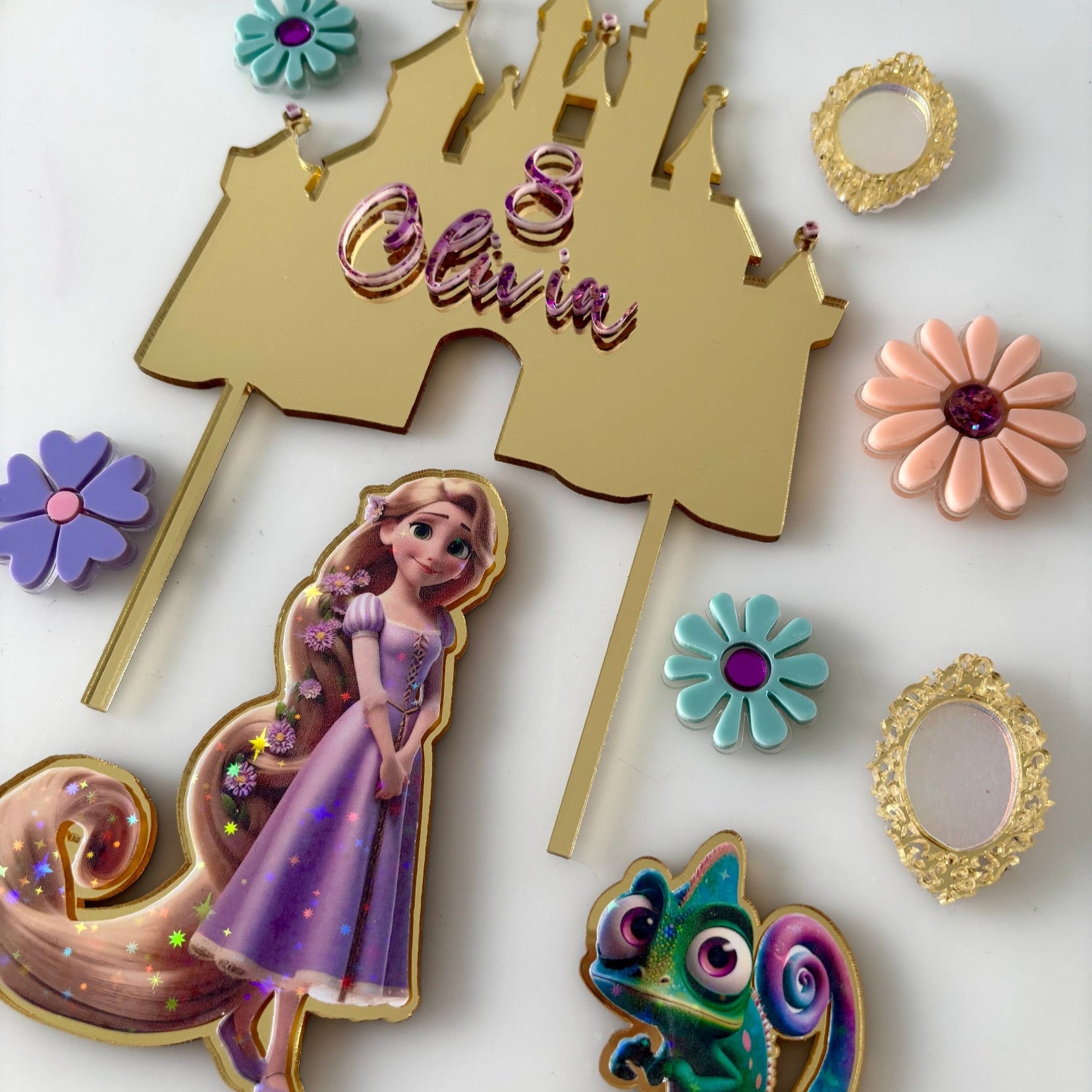 Decorative cake toppers with a castle, princess rapunzel figure, and flowers on a white background
