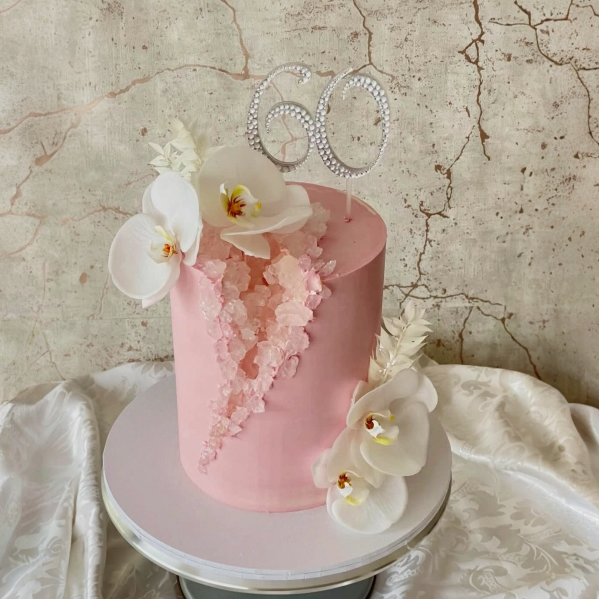Pink cake with white flowers on a marble surface with a rhinestone number cake topper