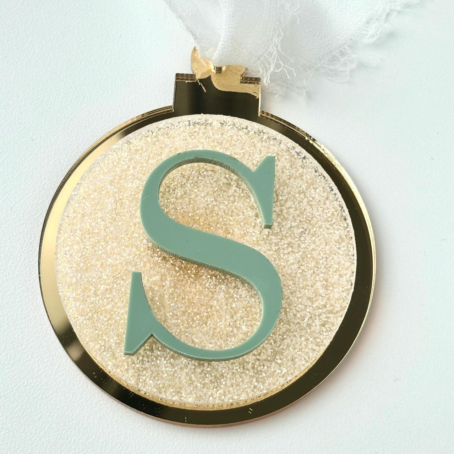 Decorative  Christmas bauble with a gold glittery background and green letter 'S' on a white background