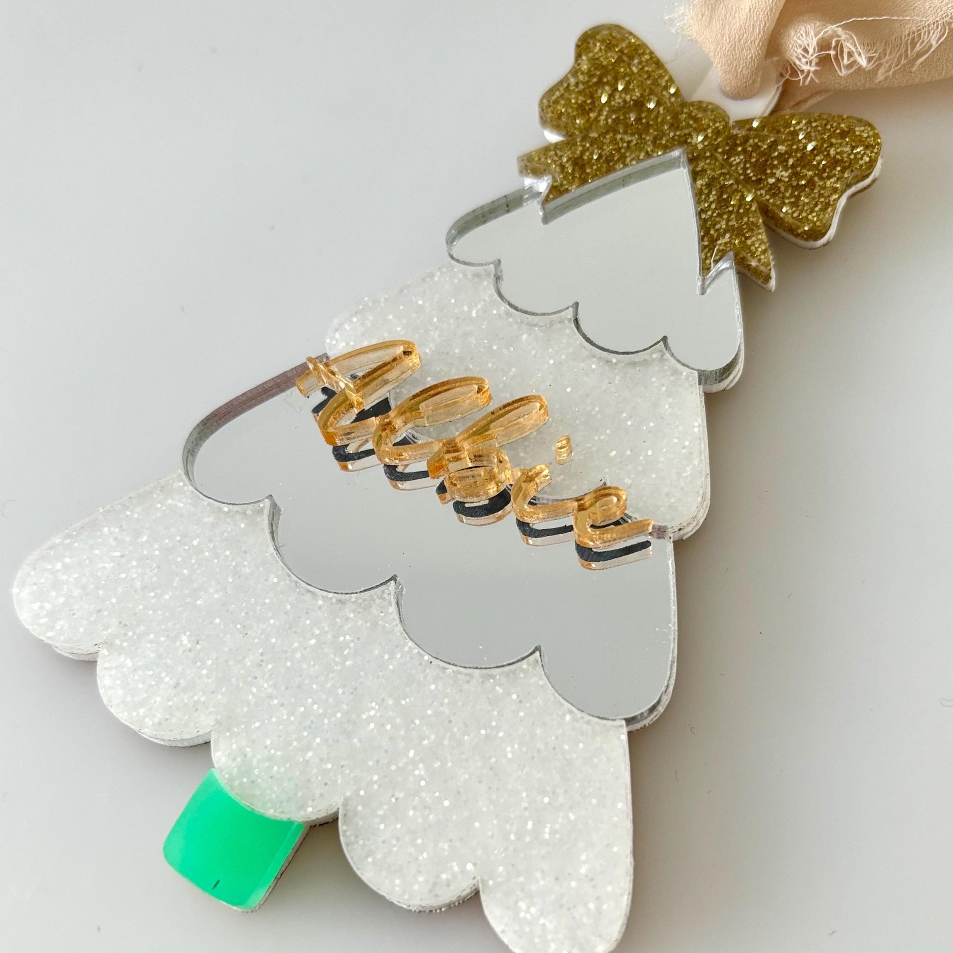 Decorative Christmas Tree ornament with gold bow and green base on a light gray background