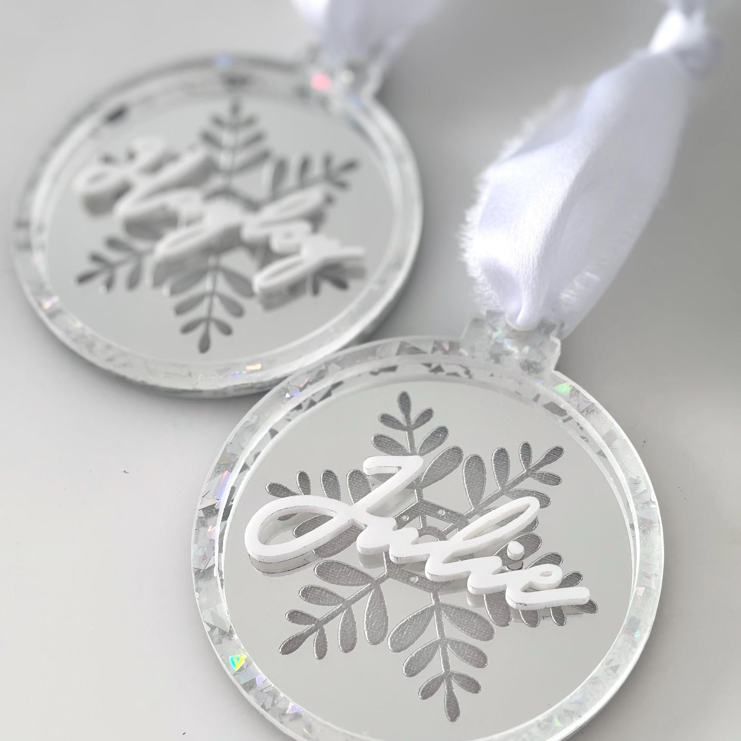 Two silver snowflake-shaped Christmas ornaments on a white background