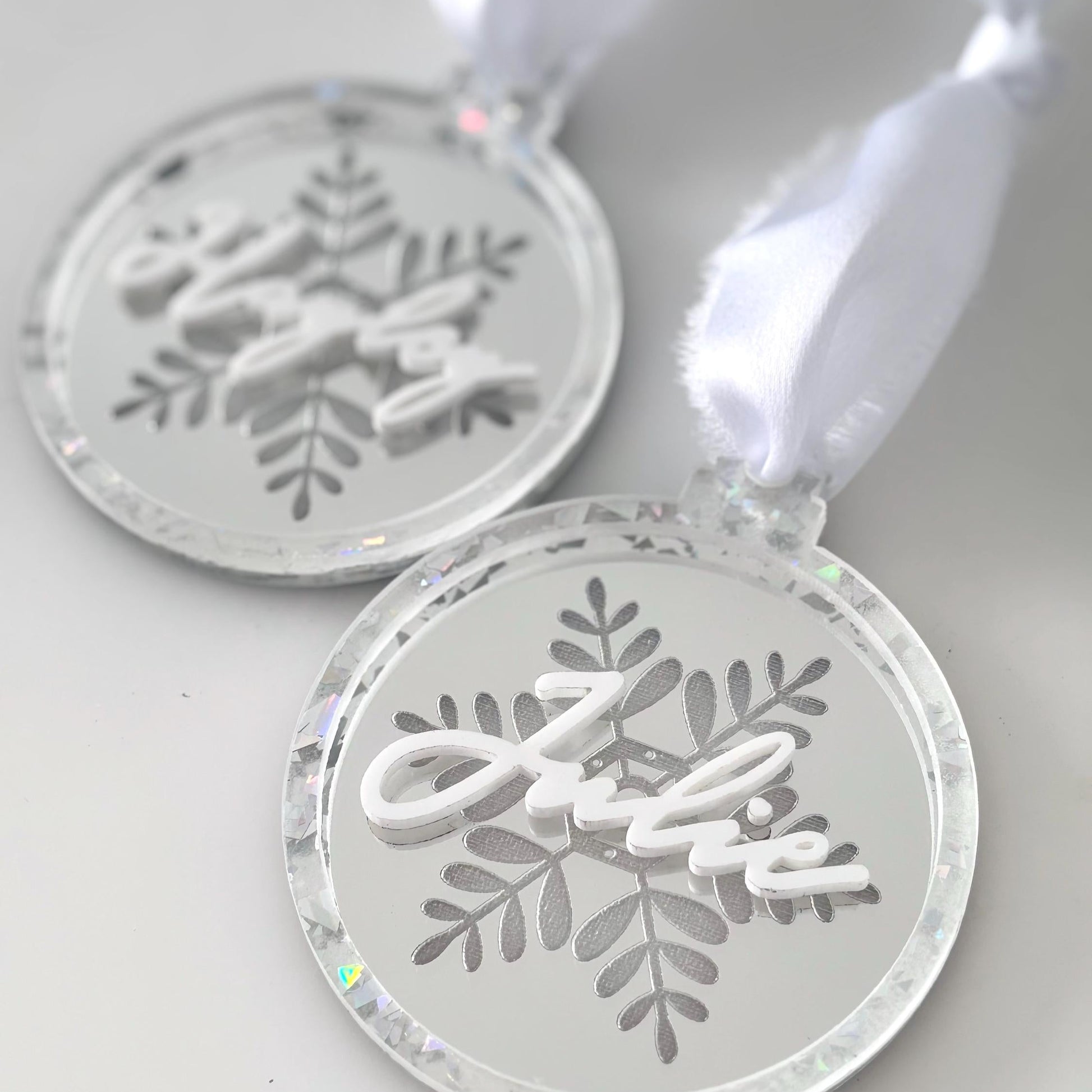 Two silver snowflake-shaped Christmas ornaments on a white background