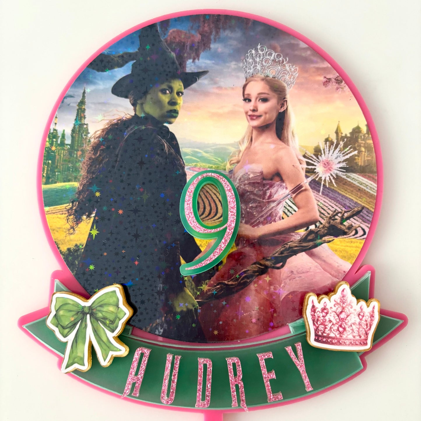 Personalised Wicked Movie themed Cake Topper, with main characters, on a pink background.