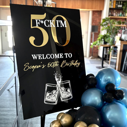 Decorative sign for a 50th birthday celebration with balloons and a casual indoor setting.