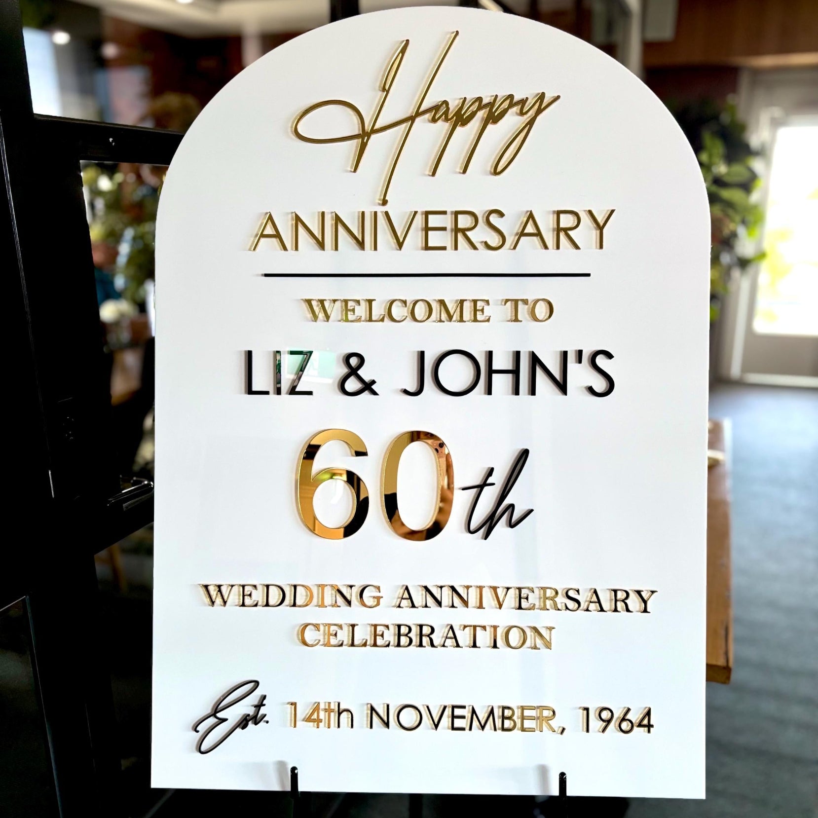 Decorative arch A1 sign for Liz & John's 60th wedding anniversary celebration in a room setting.