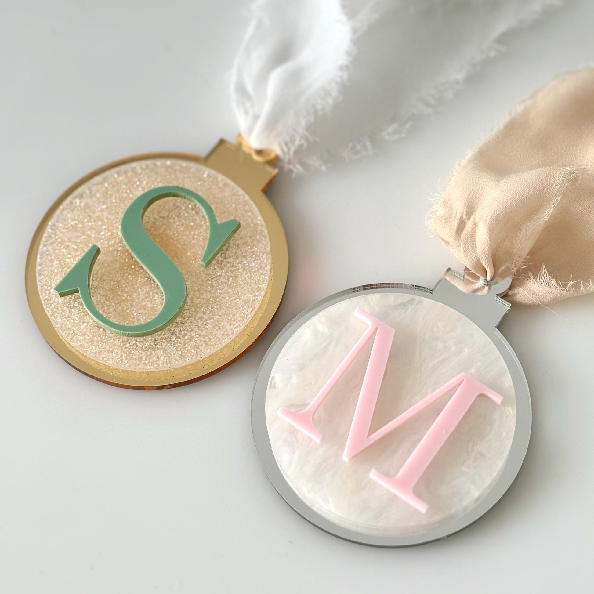 Decorative acrylic Christmas baubles with letters 'S' and 'M' on a light background