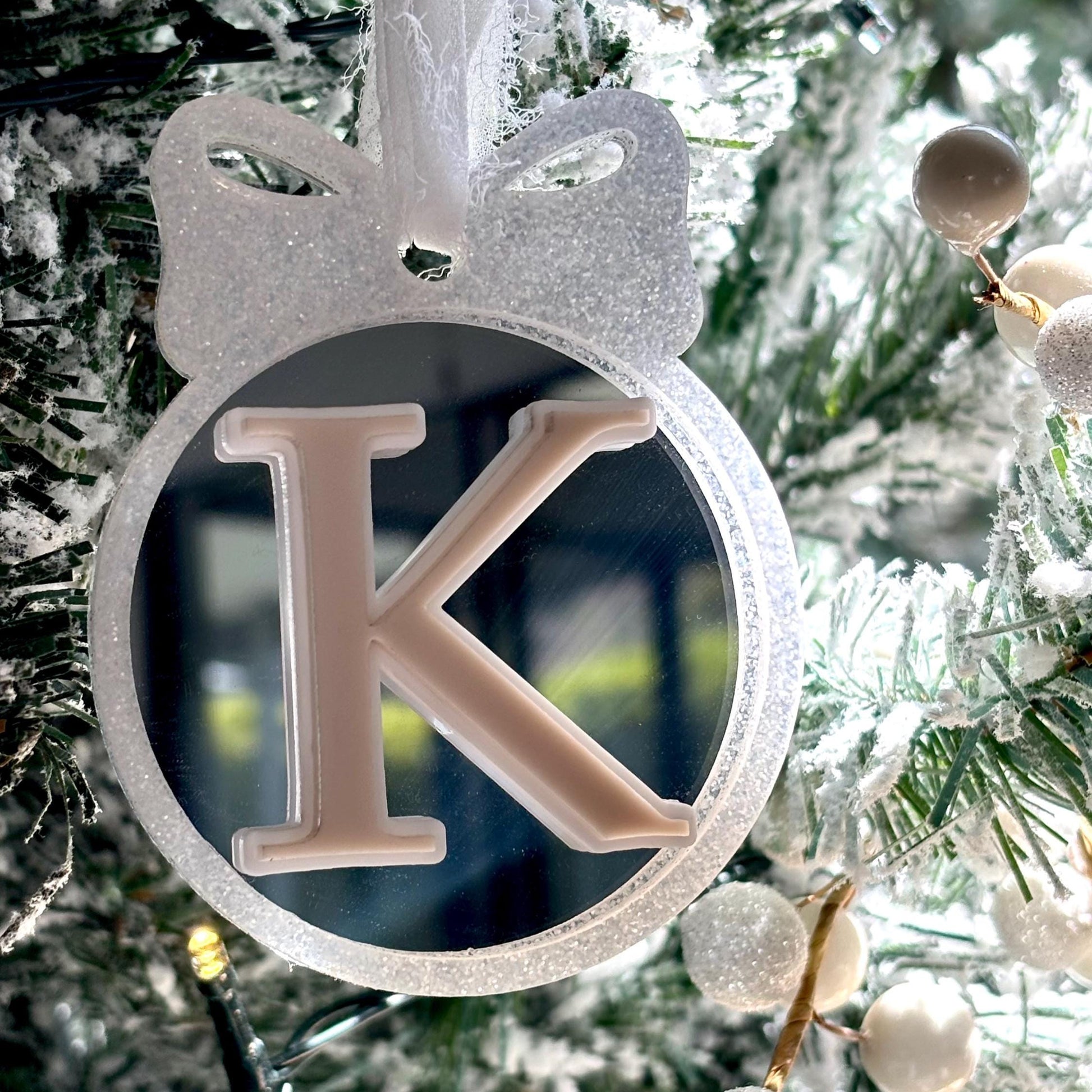 Decorative silver glitter ornament with letter 'K' hanging on a Christmas tree
