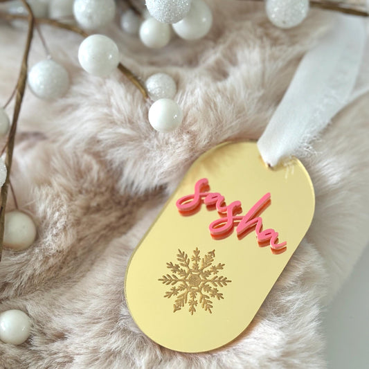 Decorative gold tag with 'Joy' in pink on a fluffy white surface with white berries.